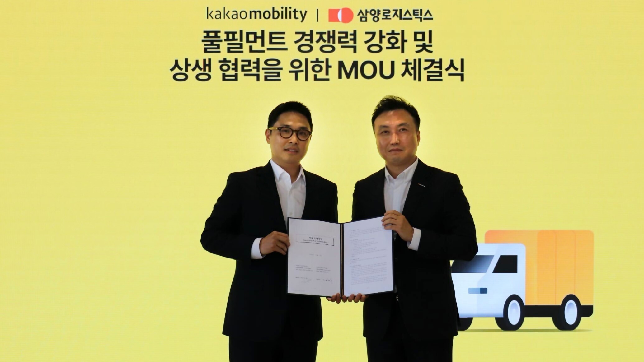 밝은 노란색 배경 앞에 양사 대표가 나란히 서서 협약서를 펼쳐 보이고 있다. 상단에는 '카카오모빌리티 | 삼양로지스틱스 풀필먼트 경쟁력 강화 및 상생 협력을 위한 MOU 체결식'이라는 문구가 적혀 있고, 오른쪽 하단에는 화물 트럭 아이콘이 그려져 있다. 두 대표 모두 검은 정장과 흰 셔츠 차림으로, 협약 체결의 상징성을 나타낸다.