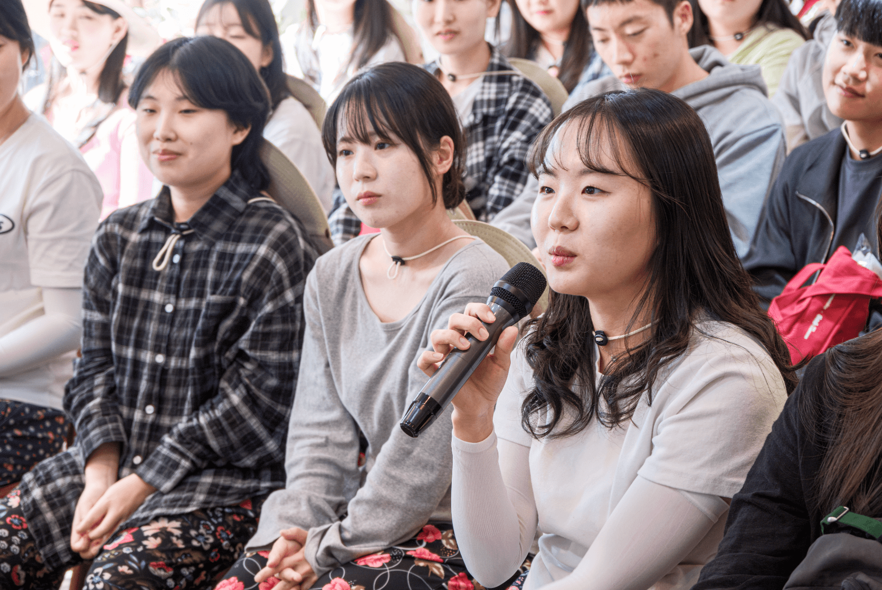 흰색 티셔츠를 입은 여성이 마이크를 들고 강연자에게 질문을 하고 있습니다.