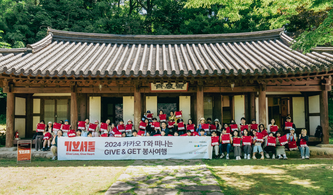 기브셔틀 1회차 기념사진으로, 봉사자들이 최태성 선생님과 함께 황희선생 유적지 앞 계단에 앉아 기브셔틀 굿즈를 들고 환하게 웃고 있다.