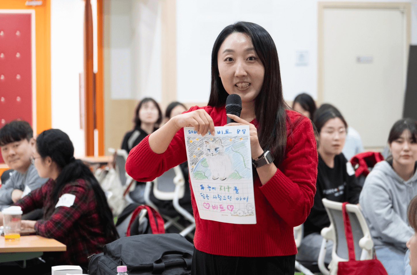 빨간색 가디건을 입은 기버분께서 자신이 작성한 입양카드 홍보물에 대해 다른 기버분들께 공유하고 있는 모습입니다.