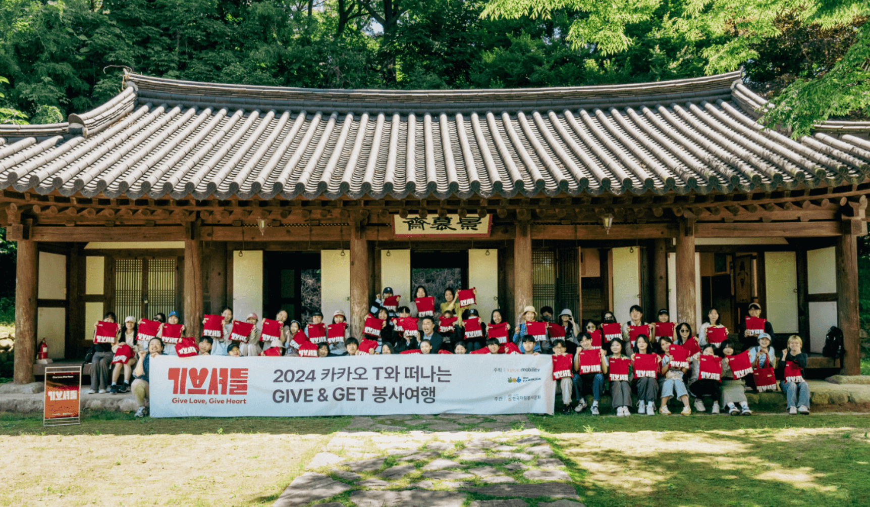 기브셔틀 1회차 기념사진으로, 봉사자들이 최태성 선생님과 함께 황희선생 유적지 앞 계단에 앉아 기브셔틀 굿즈를 들고 환하게 웃고 있습니다.