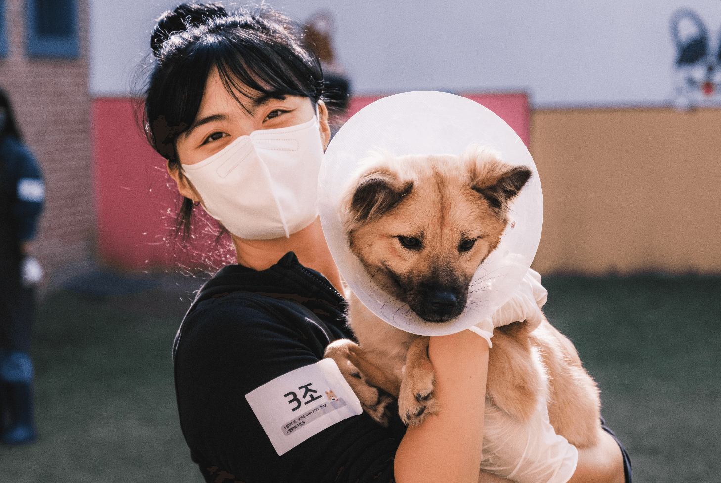 기버분께서 마스크를 낀 채 강아지를 안고 밝은 표정으로 정면을 응시하며 사진을 촬영하고 있습니다.