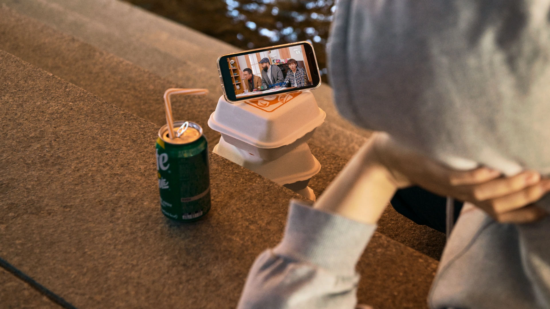 야외에서 간식과 함께 핸드폰으로 카카오TV 통해 영상을 보고 있는 사람의 사진